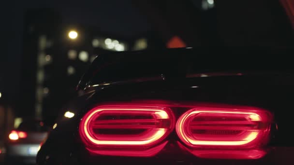 Negro coche deportivo luz trasera que brilla en la oscuridad de una ciudad nocturna, luz de estacionamiento intermitente - Imágenes, Vídeo
