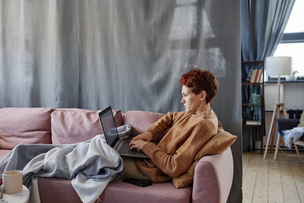 Horizontal side view shot of mature Caucasian woman having influenza staying at home working on laptop - Fotoğraf, Görsel