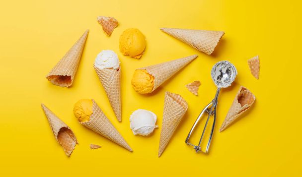 Verschiedene Eissorten in köstlichen Waffelkegeln, ein Leckerbissen für jeden Geschmacksnerv. Vor gelbem Hintergrund, flache Lage - Foto, Bild