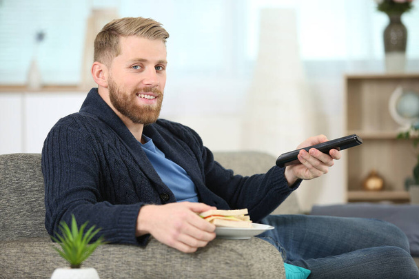 man changing tv channel with remote control while eating sandwich - Foto, immagini