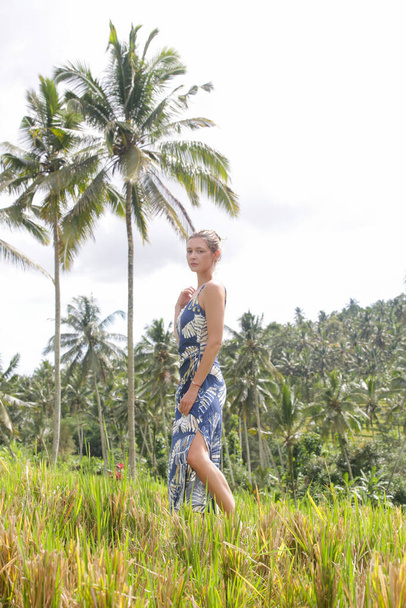 Odkryty portret młodej kobiety na polu ryżowym na tropikalnej wyspie z pięknymi palmami kokosowymi, naturalnym światłem słonecznym. Pojęcie wolności, podróżowania, środowiska, połączenia z naturą - Zdjęcie, obraz