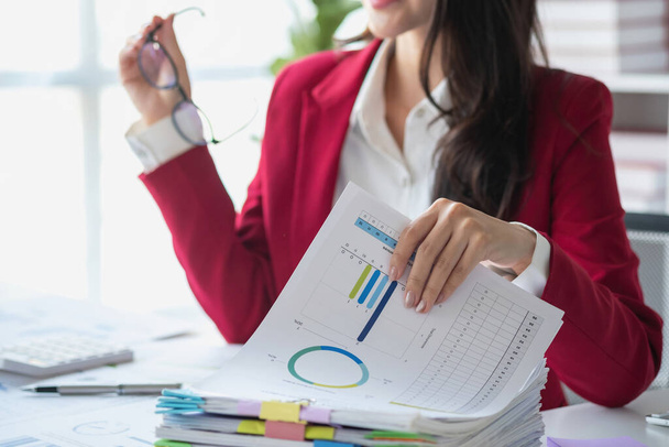 Asijská podnikatelka v červeném obleku kalkulačka firemní prodej s kalkulačkou, notebookem a tabletem na stole Interiér kanceláře businesswoman na moderním pracovišti. - Fotografie, Obrázek