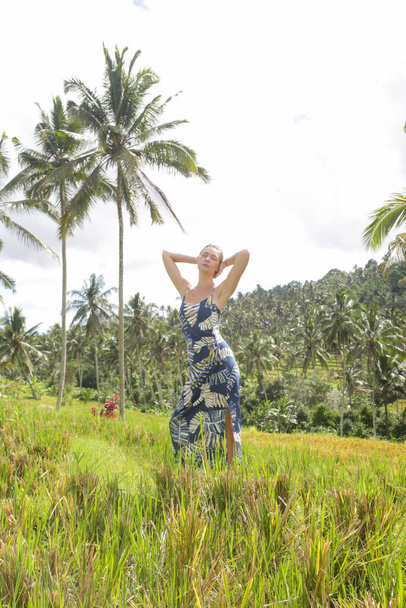 Venkovní módní portrét mladé ženy na rýžovém poli na tropickém ostrově s krásnými kokosovými palmami, přirozeným slunečním svitem. Pojem svoboda, cestování, životní prostředí, spojení s přírodou - Fotografie, Obrázek