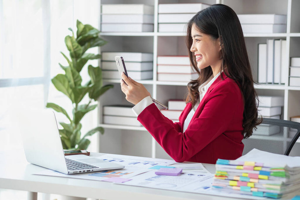 赤いスーツのアジアのビジネスマン 計算会社の販売を計算する 計算機, ラップトップ, 現代のワークステーションのビジネスマンオフィスのテーブルインテリア上のタブレット. - 写真・画像
