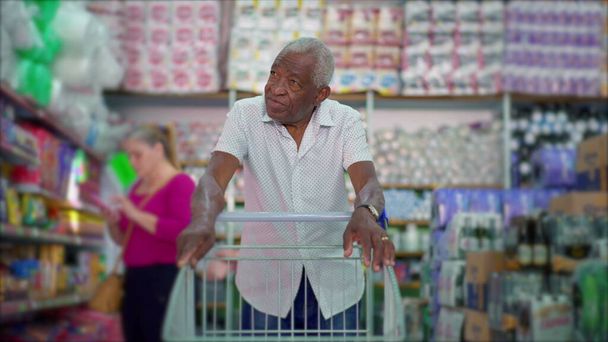 Jeden starší černý nakupující tlačí nákupní vozík v obchodě s potravinami, prohlížení výrobků na regálech zobrazující životní styl spotřebitelů - Fotografie, Obrázek