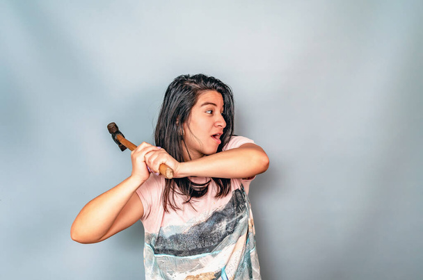 Side view woman in white shirt swings hammer. Aggressive woman with a hammer. Hispanic - Valokuva, kuva