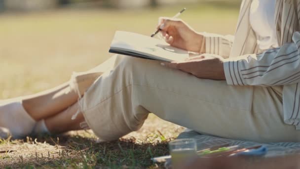 Puistossa istuva nainen, jolla on maalausharja muistikirjaa vasten. Keskimmäinen laukaus - Materiaali, video