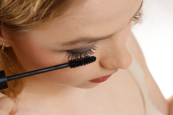 closeup of a young woman applying mascara on a white studio background - Photo, Image