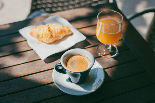 Een kop zwarte koffie, een croissant en een glas vers sinaasappelsap op een tafel in een café. Selectieve focus. Plaats voor tekst. - Foto, afbeelding