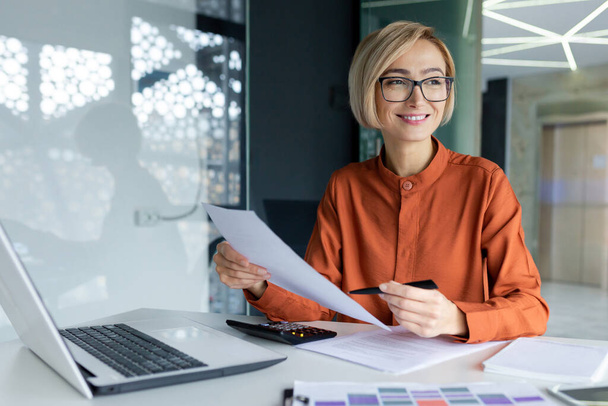 Young successful business woman working inside office with documents, woman satisfied with achievement results reviewing contract, bills and documents, financier in glasses smiling. - Photo, Image
