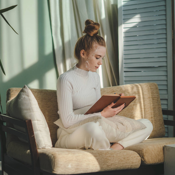 Πορτρέτο της ελκυστική χαρούμενη ονειρική γυναίκα κάθεται στον καναπέ δημιουργώντας σημειώσεις στο σπίτι σε εσωτερικούς χώρους. Γυναίκα σκέφτεται. Όμορφη νεαρή κοπέλα. Νεαρός που κρατάει μολύβι. - Φωτογραφία, εικόνα