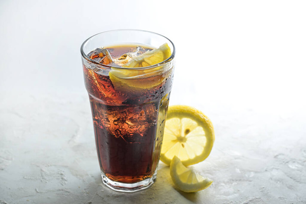 Fresh cola with ice cubes and lemon slices in a drinking glass, sweet caffeine drink against a light gray background, copy space, selected focus, narrow depth of field - Photo, image