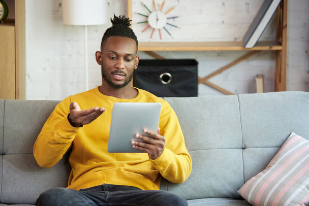 Young african man working remotely, having line video call with team, sitting on sofa at home. Online meeting with colleagues. Concept of business and education, freelance job, modern lifestyle - Valokuva, kuva