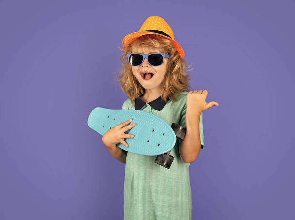 Grappig vrolijk kind in casual kleding die longboard vasthoudt en er blij en opgewonden uitziet. Studio geïsoleerd portret van kind met skateboard - Foto, afbeelding
