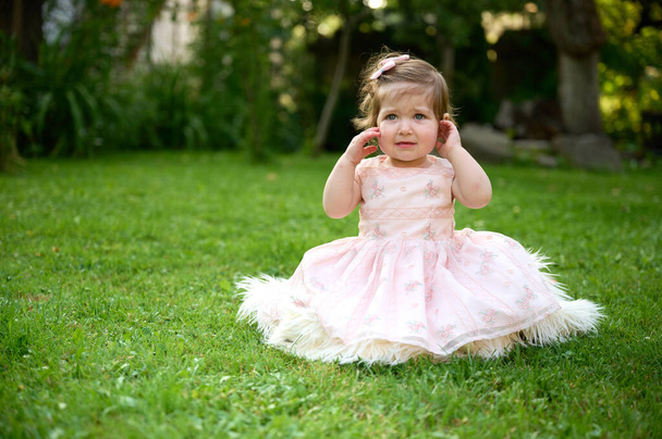 Bahçedeki çimlerin üzerinde sevimli bir kız. Portreyi kapat. Yaz manzarasında küçük mutlu bir kız. Tatlı küçük çocuk dışarıda. - Fotoğraf, Görsel