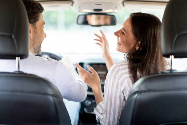 Cheerful funny young woman entertaining her husband boyfriend while going car trip together, singing songs and gesturing. Happy millennial couple enjoying auto ride, shot from back seat - Foto, afbeelding