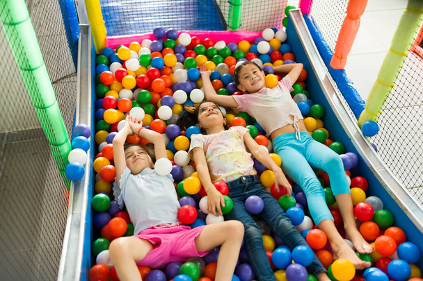 Смешные дети расслабляются, наслаждаясь игрой вместе во время отдыха на площадке для игры в мяч в помещении  - Фото, изображение