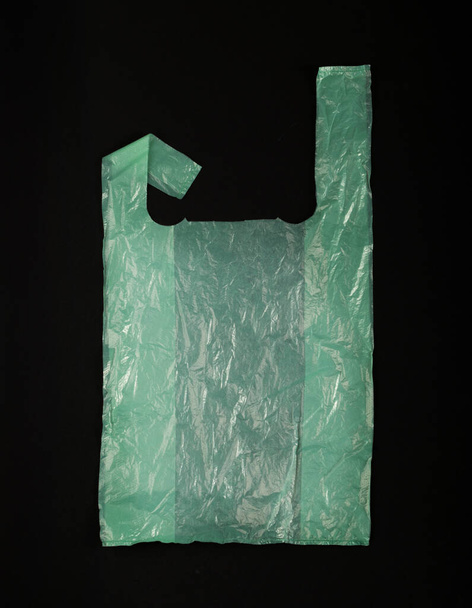Grüne Plastiktüten auf schwarzem Hintergrund, zerknüllte Plastiktüte nach dem Einkauf, Cellophan Verpackungsmüll, gebrauchte zerknitterte Einwegtasche - Foto, Bild