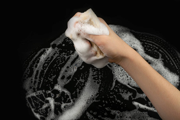 Natural Soapy Sponge with Foam, Eco Brown Sponges, Eco Friendly Hygiene Accessory, Scotch Brite Dishwasher in Hand on Black Background, Copy Space - Foto, afbeelding