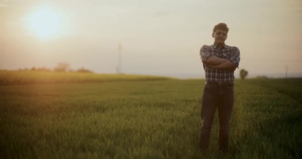 Movimiento lento del agricultor macho de pie con los brazos cruzados en forma contra el cielo durante la puesta del sol. - Metraje, vídeo