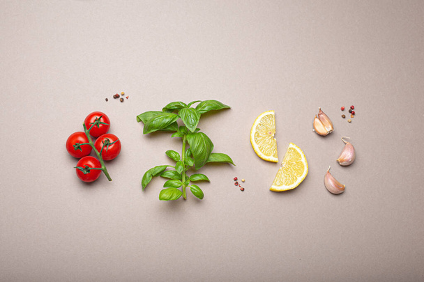 Composition with healthy food ingredients: branch of fresh cherry tomatoes, basil branch, garlic cloves, lemon wedges on minimalistic gray clean background, overhead shot - Photo, Image