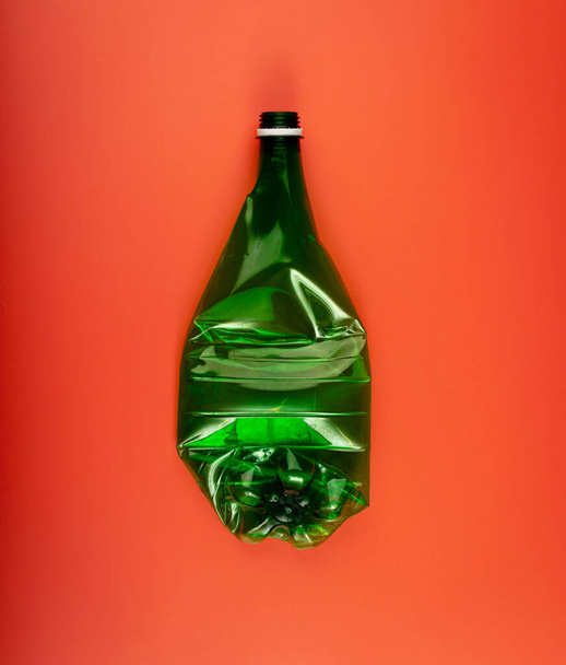 Grüne leere Plastikflasche, zerknüllte Plastikflasche, globales Umweltschutzkonzept, ausgedrückte Wasserflaschen auf rotem Hintergrund - Foto, Bild