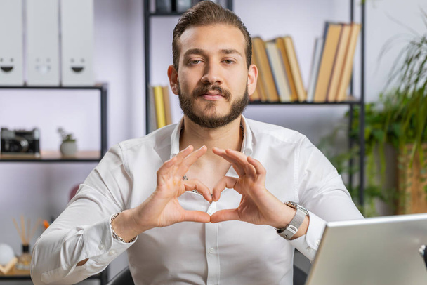 Je t'aime. Homme d'affaires libanais fait symbole de l'amour, montrant le signe du cœur à la caméra, exprimer des sentiments romantiques expriment des sentiments positifs sincères au bureau à la maison. Charité, gratitude, don - Photo, image