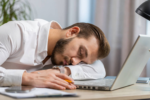 Aburrido trabajador de negocios de Oriente Medio somnoliento que trabaja en el ordenador portátil, apoyado en la mano que se duerme en la oficina. Hombre libanés adicto al trabajo cansado y cansado. Empleo, ocupación sin trabajo - Foto, imagen