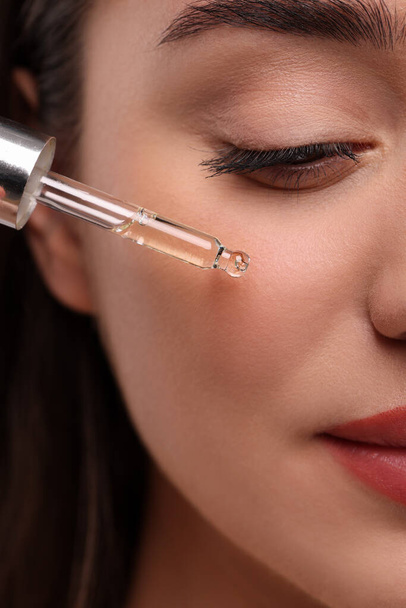 Young woman applying essential oil onto face, closeup - Fotografie, Obrázek