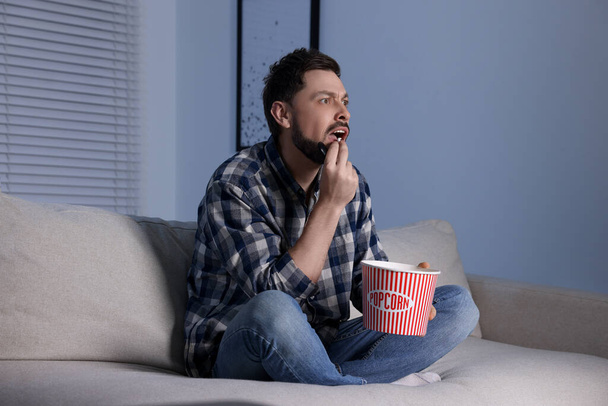 Emotional man eating popcorn while watching TV at home in evening - Фото, зображення