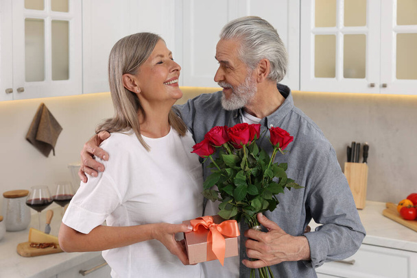 Happy affectionate senior couple with gift box and beautiful bouquet indoors - Foto, afbeelding