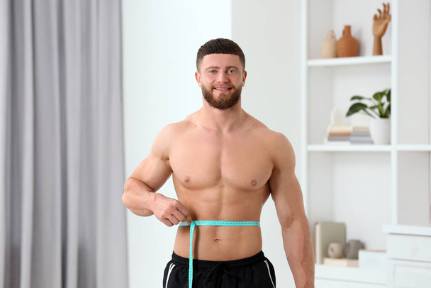 Portrait of happy athletic man measuring waist with tape at home. Weight loss concept - Foto, Imagem