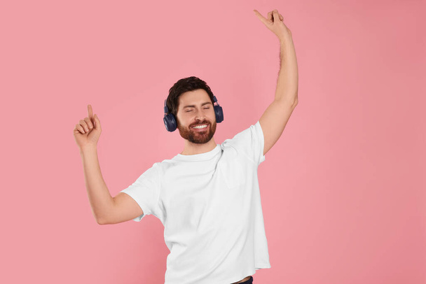 Happy man listening music with headphones on pink background - Photo, image