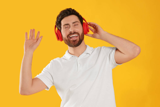 Happy man listening music with headphones on yellow background - Фото, зображення