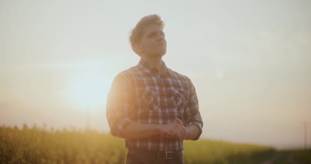 Langzame beweging van contemplatieve mannelijke boer staande in boerderij tegen de hemel tijdens zonsondergang. - Video