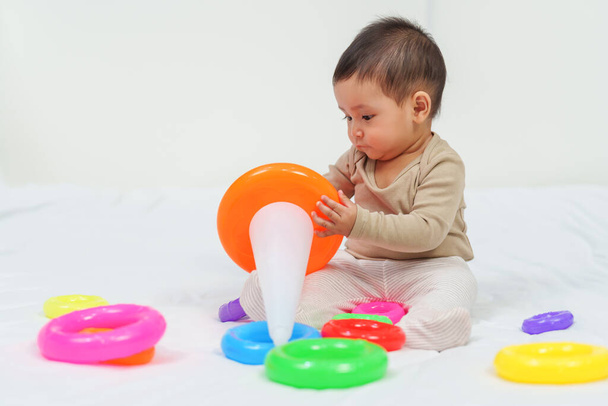 infant baby playing the pyramid toy with colored rings on a bed - Foto, Imagem