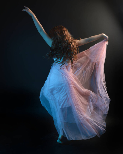 Ritratto a figura intera di una bella ballerina bruna, che indossa un abito etereo, ballando con un tessuto fluente. isolato su sfondo scuro studio con illuminazione cinematografica colorata. - Foto, immagini