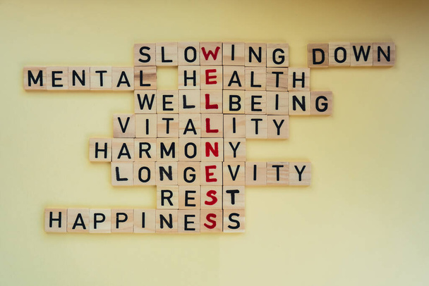 Top view of WELLNESS word on yellow background. Minimalism creative crossword puzzle concept. Message of text Slowing down mental health wellbeing vitality harmony longevity rest happiness. Supportive - Photo, Image