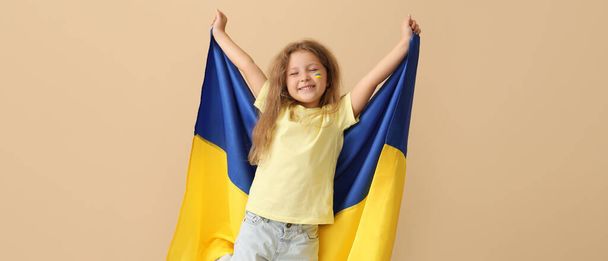 Little girl with flag of Ukraine on beige background - Foto, imagen