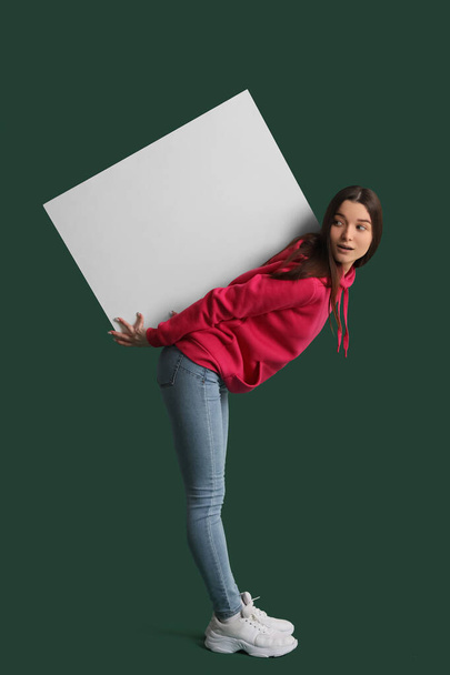Young woman in hoodie with big blank poster on green background - Foto, Imagem