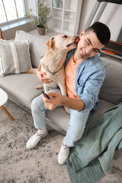Молодий чоловік з гарненьким собакою дивиться телевізор на дивані вдома. - Фото, зображення