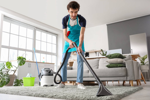 Young man hoovering carpet at home - Foto, afbeelding