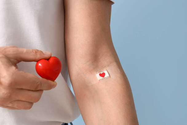 Mature blood donor with heart and applied medical patch on blue background, closeup - Photo, image