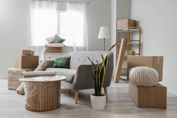 Sofá con mesa envuelta y cajas de cartón en la sala de estar en el día en movimiento - Foto, imagen