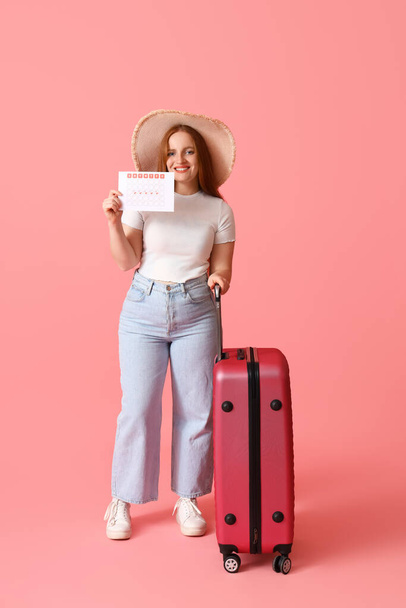Νεαρή γυναίκα με ημερολόγιο εμμήνου ρύσεως και βαλίτσα σε ροζ φόντο - Φωτογραφία, εικόνα