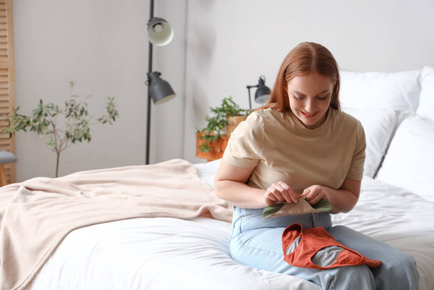 Mujer joven con almohadilla menstrual reutilizable en el dormitorio - Foto, Imagen