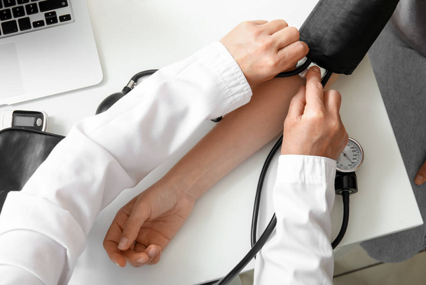 Жінка-лікар, яка вимірює кров'яний тиск пацієнта за столом у клініці, вид зверху - Фото, зображення