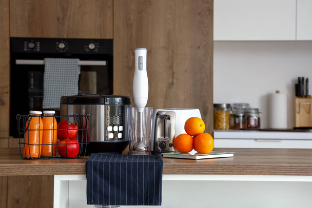 Çoklu fırın, blender, tost makinesi ve portakallı teraziler mutfaktaki ahşap masada. - Fotoğraf, Görsel