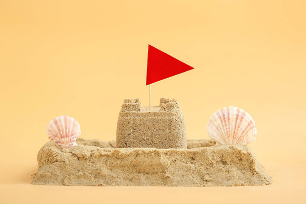 Castle made of sand with seashells and flag on orange background - Fotó, kép