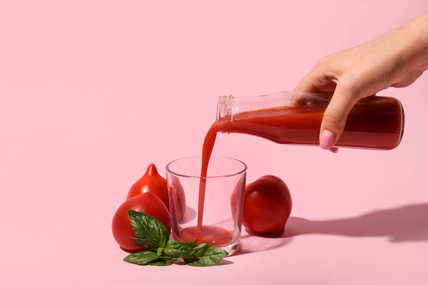 Woman pouring tasty tomato juice from bottle into glass on pink background - Фото, изображение
